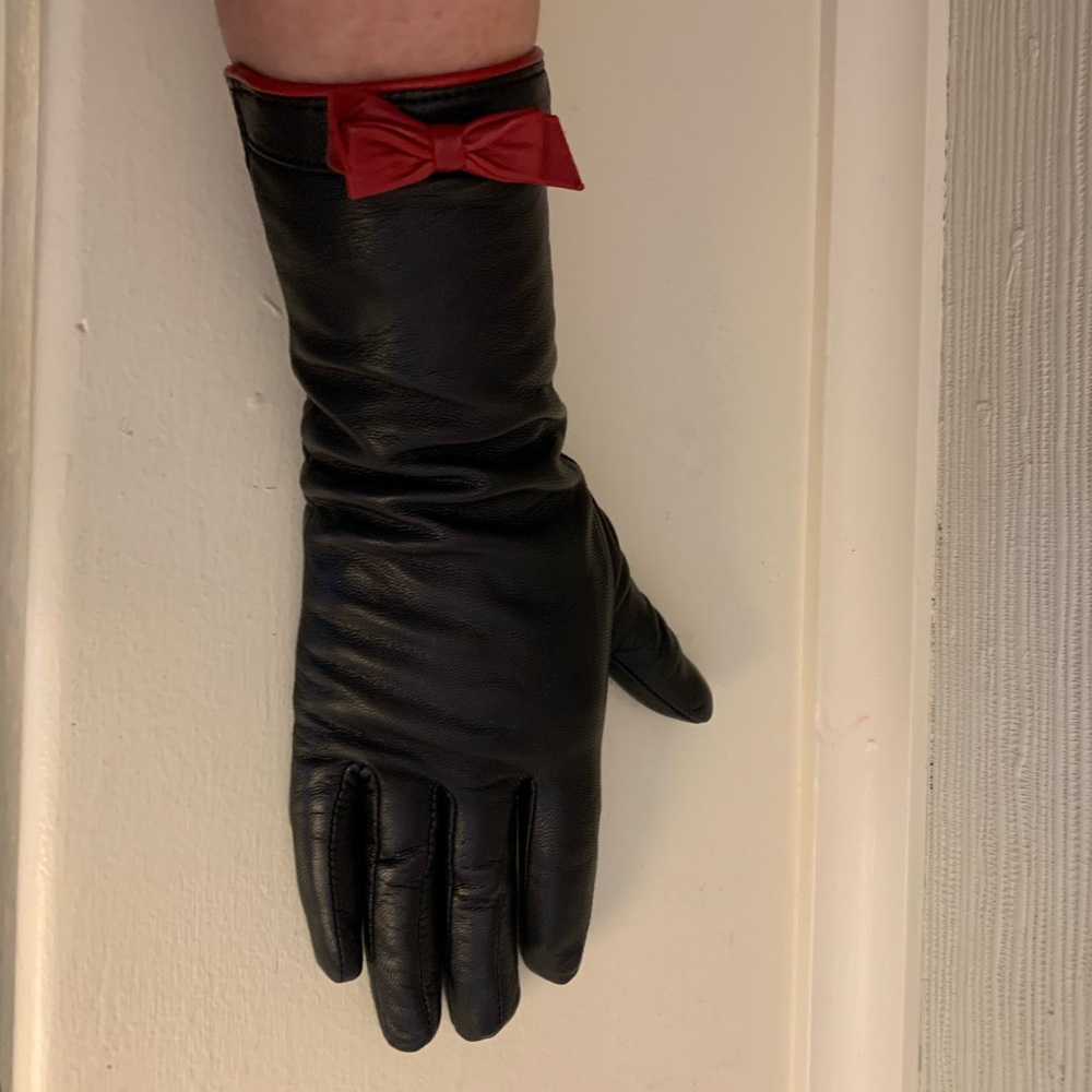 Above the wrist black leather gloves with red leather details and snaps